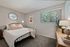 Cozy bedroom with modern decor, featuring a plush bed, elegant wall art, and natural light streaming through large windows, adding warmth to the space.