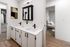 Modern apartment bathroom with dual sinks, sleek black fixtures, and a view into a cozy bedroom with stylish decor.