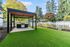 Charming backyard with lush green lawn, sleek pergola, and modern outdoor grill, enclosed by a classic white picket fence and vibrant garden.