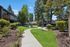 Charming apartment complex with lush greenery, winding paths, and modern outdoor seating area under tall trees.