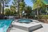 Inviting outdoor pool and spa area with sun loungers in a lush, green apartment complex with beautiful trees.