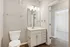 Modern bathroom with elegant vanity, sleek fixtures, and spacious mirror, seamlessly connecting to a cozy carpeted room.