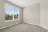 Bright and inviting empty room with plush carpet and a large window offering a pleasant view of lush greenery.