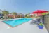 Inviting apartment complex with a sparkling outdoor pool surrounded by lounge chairs and vibrant red umbrellas, promising a luxurious and relaxing lifestyle.