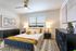 Elegant bedroom featuring a stylish blue bed with modern abstract art, cozy lighting, and chic decor for a serene retreat.