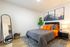 Inviting bedroom with vibrant orange accents, elegant wall art of mountains, and modern decor featuring a full-length mirror and lush plant.