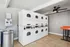 Modern and efficient laundry room with stacked washers and dryers, sleek stainless steel trash bin, and stylish ceiling fan.