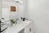 Elegant bathroom interior featuring a modern white vanity with sleek black fixtures, complemented by greenery and stylish decor.