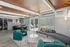 Modern and inviting living area with stylish teal armchairs, a sleek white table, and a cozy sofa near a sunlit pool view.