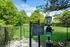 Inviting green dog park with secure fencing and convenient pet waste stations, surrounded by lush trees and sunny skies.