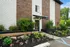 Inviting apartment building exterior with beautiful brick facade, lush green landscaping, and vibrant flower beds, showcasing modern living.