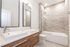 Modern bathroom featuring dual sinks, sleek wood cabinetry, and a glass-enclosed shower-tub combo for a luxurious feel.
