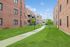 Charming apartment complex with inviting red brick exteriors, lush green lawns, and a serene pathway perfect for leisurely strolls.