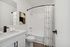 Chic and modern bathroom with sleek white finishes, elegant black hardware, and contemporary geometric shower curtain, offering a stylish and inviting space.