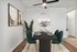 Elegant dining area with dark wood table, teal velvet chairs, and modern art. Features a chic round mirror and ceiling fan, creating a stylish and inviting space.