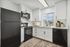 Modern kitchen with sleek black appliances, elegant white cabinetry, and large window allowing natural light to brighten the space.