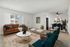 Modern living room with stylish decor, featuring a cozy brown couch, chic blue chairs, and a marble coffee table. Open dining area with elegant dark table and plush green chairs, perfect for entertaining.