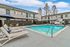 Inviting apartment complex courtyard featuring a sparkling pool with lounge chairs, surrounded by modern two-story buildings under a vibrant blue sky.