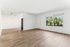 Bright open living space with natural light, featuring elegant wood flooring and a view of lush greenery through a large window.