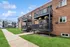 Charming brick apartment exterior with private balconies, lush green lawns, and vibrant hanging plants, perfect for modern living.
