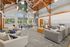 Spacious modern lounge area with high ceilings, featuring elegant wooden beams and abundant natural light. Includes comfortable gray sofas, stylish d&eacute;cor, and a large communal table with views of lush greenery outside.