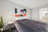 Modern bedroom showcasing elegant decor with abstract art, cozy bedding, stylish lighting, and a glimpse into a spacious bathroom.
