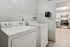 Modern laundry room with sleek white washer and dryer, leading into a stylish kitchen with stainless steel appliances and bright cabinetry.