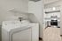 Modern apartment laundry room with a sleek washer and dryer set, leading into a bright kitchen with stainless steel appliances and white cabinetry.