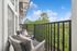 Inviting balcony with cozy seating offering a serene view of lush green trees under a clear blue sky.