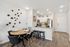 Modern dining and kitchen area featuring sleek black chairs, decorative wall art, and a contemporary kitchen with stainless steel appliances.