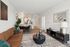 Modern open-concept living space featuring a stylish brown leather sofa, chic coffee table, elegant dining area, and a sleek kitchen with stainless steel appliances.