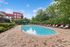 Inviting outdoor pool area surrounded by lush greenery, stylish red and white loungers, and modern urban buildings in the background.