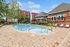 Inviting apartment community pool area with sun loungers, surrounded by lush greenery and charming brick architecture.