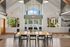 Bright, modern living area with high ceilings, featuring a welcoming dining table and large windows offering a stunning view of lush greenery and a sparkling pool.