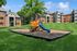 Charming apartment complex with a vibrant playground, lush green lawns, and welcoming architecture under a clear blue sky.