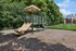 Charming outdoor playground with a slide, surrounded by lush greenery and open green space, perfect for family fun.