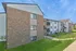 Charming apartment building with a beautiful brick facade and modern balconies, nestled in a serene green environment with clear blue skies.