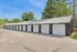 Well-maintained row of modern garages with sleek white doors and black trims, surrounded by lush greenery and blue skies.
