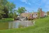 Charming lakeside apartment complex featuring a picturesque pond with a central fountain, surrounded by lush greenery and sunny skies.