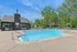 Inviting outdoor pool area with lounge chairs and shaded seating, surrounded by lush greenery and a modern clubhouse under a bright blue sky.