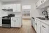 Bright and modern kitchen with sleek white cabinetry, stainless steel appliances, and hardwood flooring, leading to a sunlit dining area with large windows.