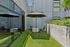 Charming outdoor patio with lush green turf, modern seating, and a stylish umbrella, offering a serene urban retreat.