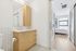 Modern bathroom with light wooden cabinetry leading to a cozy, sunlit bedroom through sliding doors.