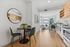 Modern apartment interior showcasing a stylish open-concept kitchen and dining area with light wood flooring, sleek furnishings, and vibrant art piece.