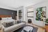 Modern bedroom with stylish decor featuring a cozy bed, sleek gray sofa, abstract art, and large windows offering natural light.