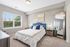 Bright and inviting bedroom with a plush blue headboard, elegant decor, and large window offering natural light and scenic views.