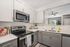 Modern kitchen with sleek stainless steel appliances, elegant white and gray cabinetry, and open view to a bright living room.
