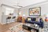 Modern living room with stylish decor, featuring a cozy blue sofa, chic armchair, vibrant artwork, and a sleek open kitchen with bar seating.
