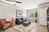 Inviting living room with modern decor, featuring a plush blue sofa, stylish armchair, and vibrant artwork. Natural light fills the space, highlighting the chic geometric rug and elegant wooden accents.