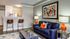 Modern living room with navy sofa, vibrant orange accents, and a sleek open-concept kitchen. Elegant artwork and ambient lighting create a cozy, stylish space.